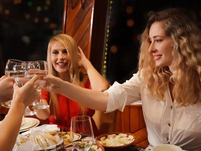 Two female tourists toasting with drinks on the deck of an Abu Dhabi dhow dinner cruise