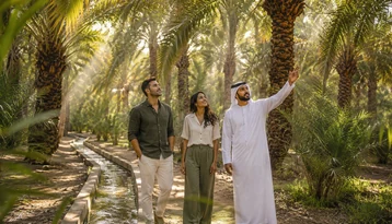 Emirati guide showing visitors the date palms and traditional falaj irrigation channel at Al Ain Oasis
