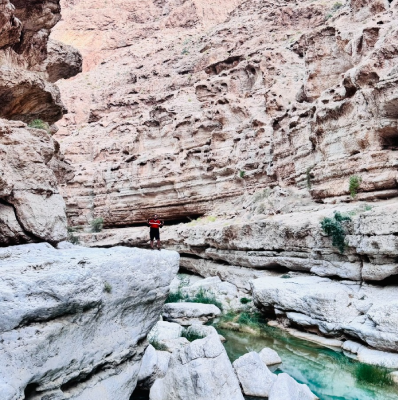 Seyed Shifaam standing on a rock ledge above turquoise pools inside Wadi Shab canyon, Oman
