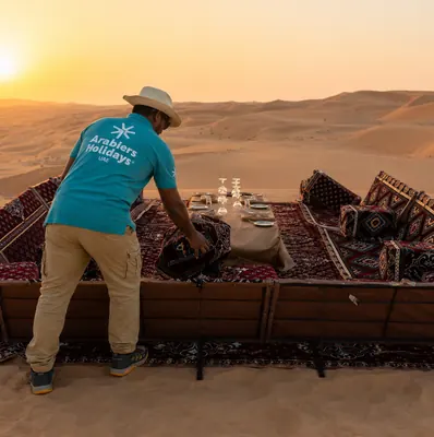 Mujeeb Rahman preparing a private desert dinner majlis with cushions, carpets and table settings at sunset for Arabiers guests in Abu Dhabi