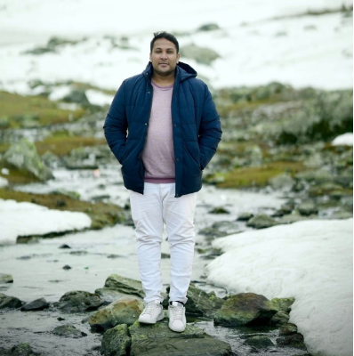Seyed Shifaam standing on rocks beside a stream in a snow-covered valley in Kashmir
