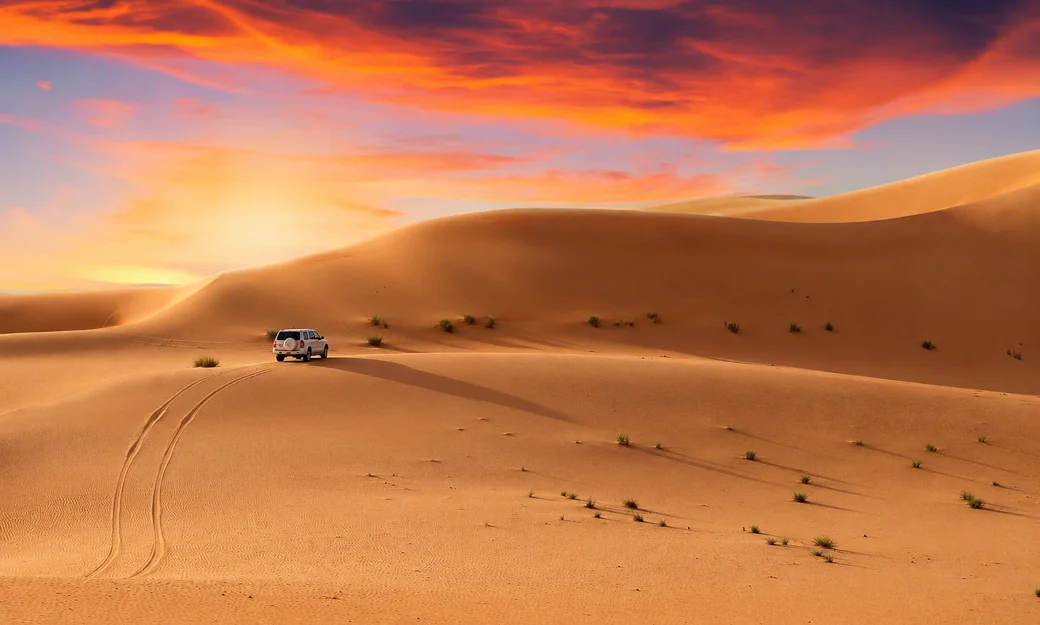 4x4 vehicle driving across golden desert dunes at sunset in Abu Dhabi