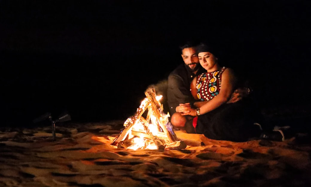 Couple sitting beside a bonfire during their Liwa overnight camping experience