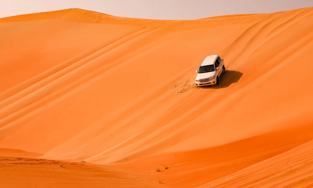 White Toyota Land Cruiser kicking up sand while driving across the Liwa desert dunes