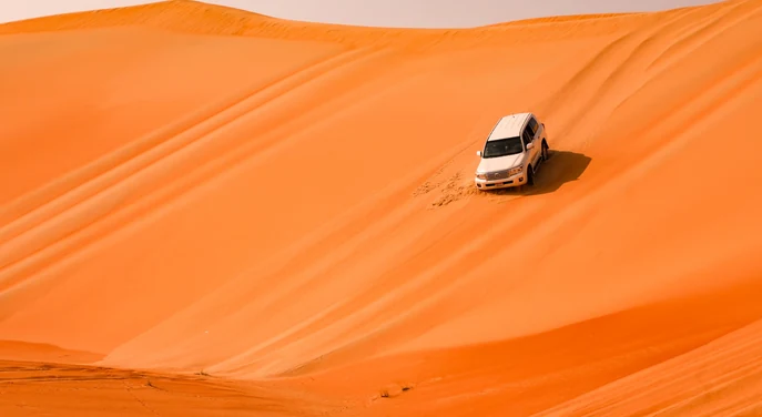White Toyota Land Cruiser kicking up sand while driving across the Liwa desert dunes