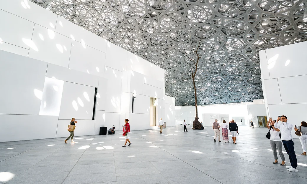 Visitors beneath the geometric dome inside Louvre Abu Dhabi