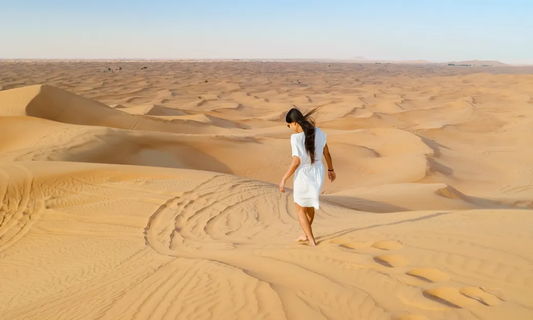 Traveller walking alone across quiet Abu Dhabi dunes