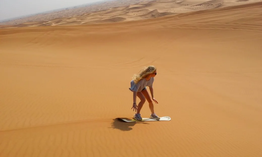 Woman enjoying sandboarding on a desert dune in Abu Dhabi