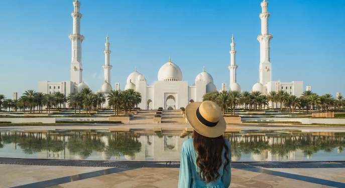 A visitor facing Sheikh Zayed Grand Mosque across the reflecting pool