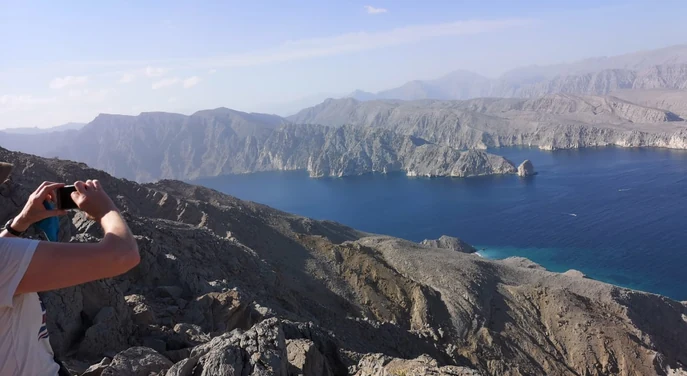 Traveller photographing the fjords from a rocky Jebel Sham viewpoint in Musandam