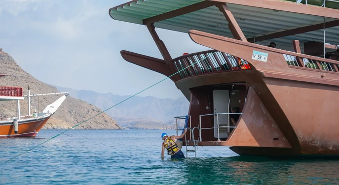 Guest entering the water from a traditional dhow during a Khasab swimming stop