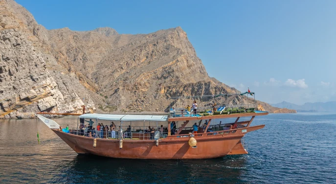 Guests aboard a traditional dhow cruising beside the rugged mountains of Khasab