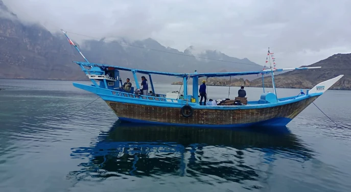 Traditional blue dhow anchored on calm water beneath the Musandam mountains