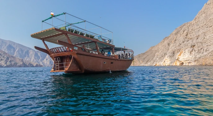 Traditional wooden dhow cruising between the dramatic mountains of Khasab