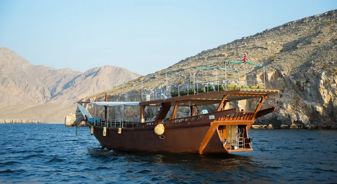 Traditional wooden dhow sailing beside the rocky mountains of Musandam