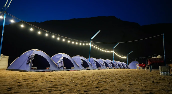 Row of illuminated camping tents on a remote Musandam beach at night