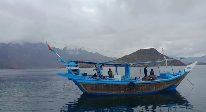 Traditional dhow anchored on calm water beneath cloudy Musandam mountains