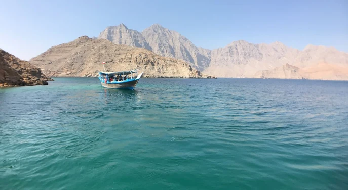 Dhow boat on turquoise water surrounded by Musandam mountains