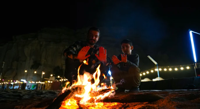 Guests warming themselves beside a campfire at a Musandam overnight beach camp