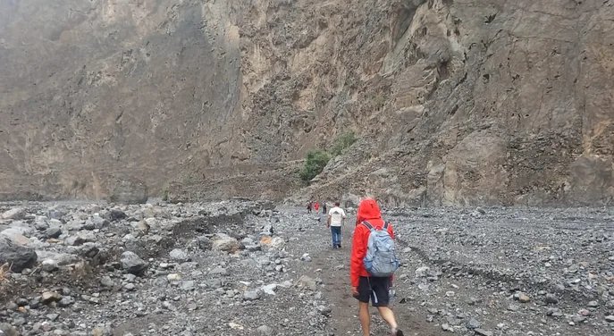 Hikers walking through the rocky canyon floor of Wadi Ain