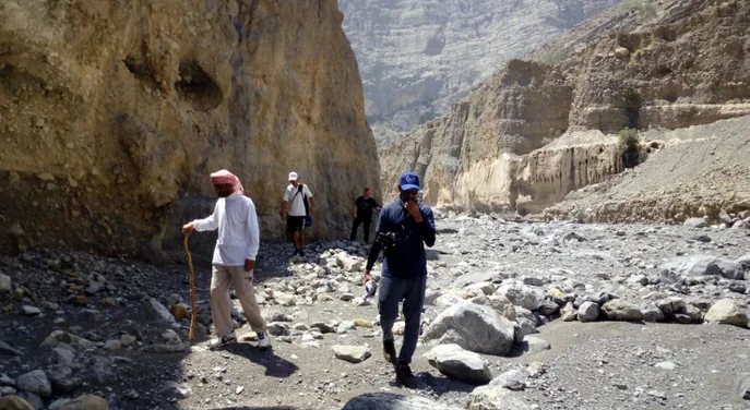Guided hikers walking along the rugged Wadi Ain riverbed