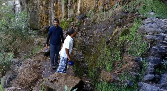 Travellers beside the green rock wall and flowing water in Wadi Ain