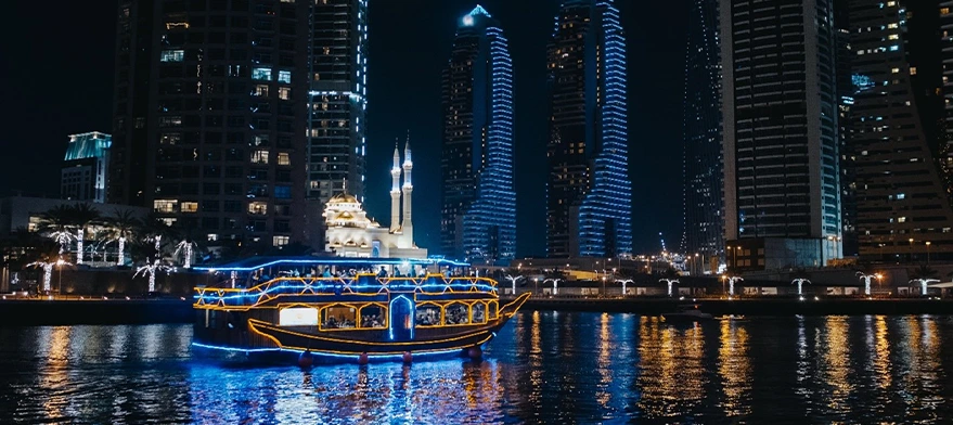 Traditional dhow sailing past heritage buildings on Dubai Creek at dusk