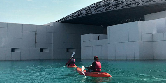 Kayakers paddling on the water beside the domed Louvre Abu Dhabi museum