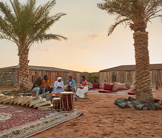 Guests around a fire at a Bedouin desert camp at sunset on a Ras Al Khaimah desert safari